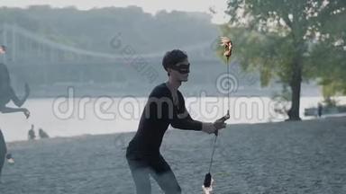 年轻苗条的男人穿着黑色的衣服，女人站在河岸上用火焰<strong>表演节目</strong>。 熟练的射击技巧